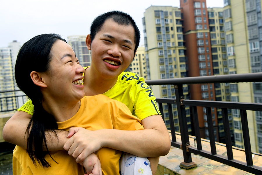 2021年8月17日，王倩（左）背着弟弟在公租房楼顶平台上看楼外的风景。这时，弟弟会很开心。